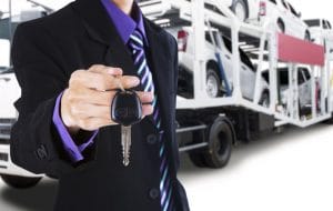 Person standing in front a vehicle transporting truck with keys in hand, car transportation by truck, companies that transport cars